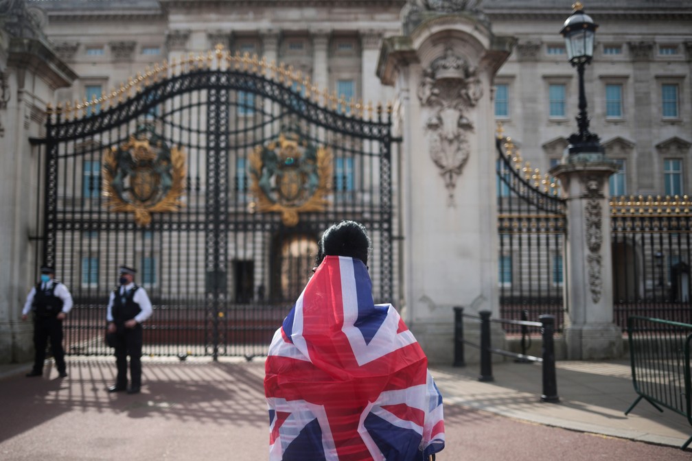 Pessoa enrolada na bandeira britânica olha para o Palácio de Buckingham após o anúncio da morte do prince Philip, marido da rainha Elizabeth II, em 9 de abril de 2021 — Foto: Hannah McKay/Reuters