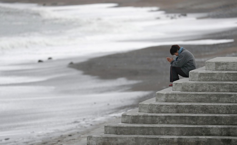 11 de março - Uma mulher reza pelas vítimas do terremoto e tsunami de 11 março de 2011 em Iwaki, no Japão — Foto: Kyodo/via Reuters