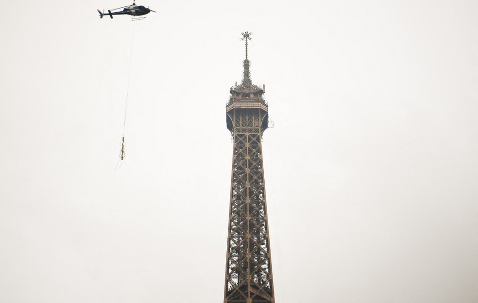 Helicóptero carrega antena que foi colocada no topo da Torre Eiffel e deixou o monumento 6 metros mais alto — Foto: Christophe Archambault/AFP