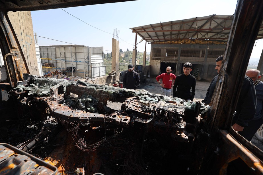 Homens olham para veículo queimado em ataque de colonos israelenses na cidade palestina de Huwara, na Cisjordânia