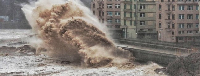 Ondas atingem um paredão em frente a edifícios em Taizhou, província de Zhejiang, leste da China. Os mesmos oceanos que nutriram a evolução humana estão prontos para desencadear a miséria em escala global alerta um projeto de relatório da ONU  — Foto: AFP