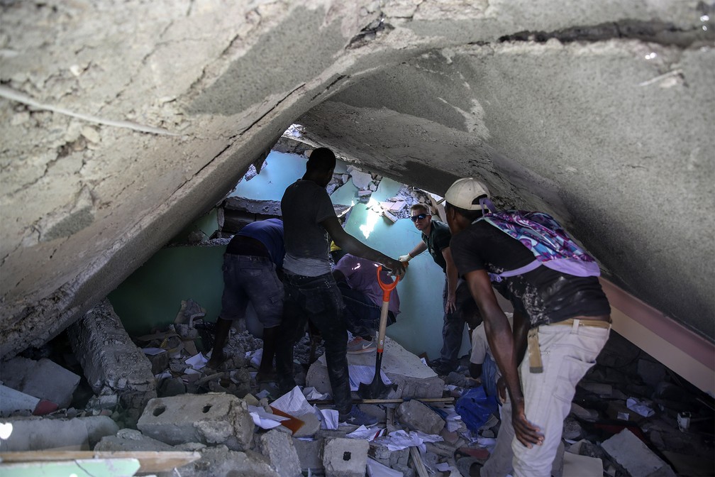 Grupo procura sobreviventes em uma casa destruída pelo terremoto em Les Cayes, Haiti — Foto: Joseph Odelyn/AP