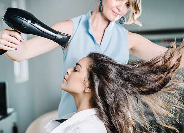 mulher jovem e bonita usando secador de cabelo no salão de