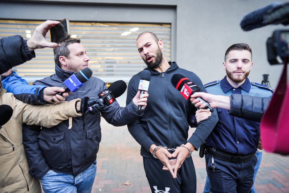 Andrew Tate conversa com a mídia enquanto é levado pela polícia romena; ele está preso desde 29 de dezembro acusado de estupro e tráfico humano