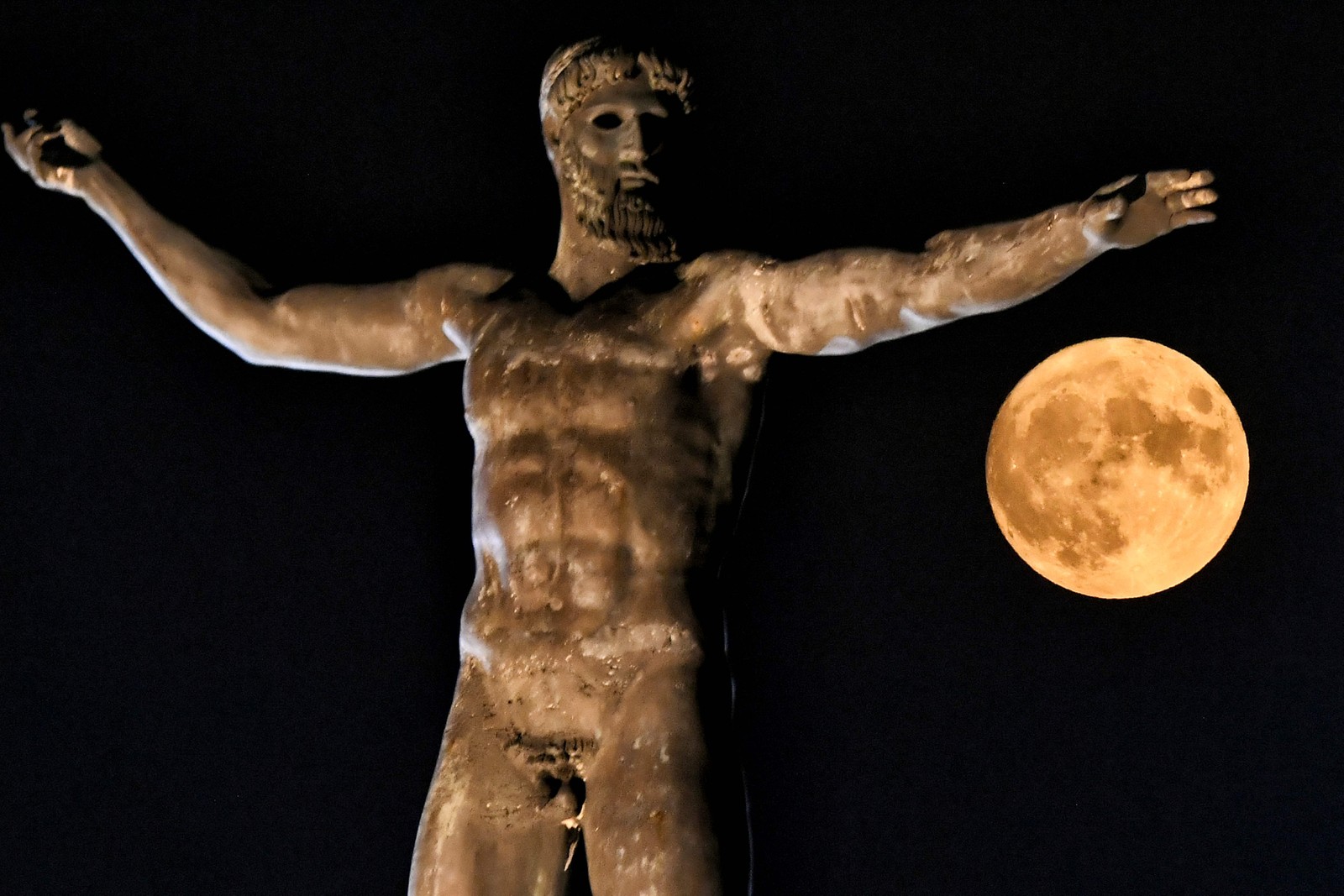 Lua cheia é fotografada próximo ao braço da estátua do antigo deus grego Poseidon, na antiga Corinto, perto de Atenas  — Foto: VALERIE GACHE / AFP