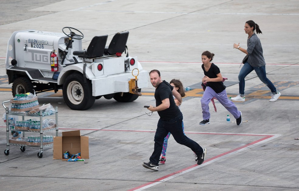 Pessoas correm na pista do Aeroporto Internacional de Fort Lauderdale-Hollywood, na Flórida, nos EUA, após um atirador abrir fogo dentro do terminal 2. Cinco pessoas morreram e oito ficaram feridas no ataque (Foto: Wilfredo Lee/AP)
