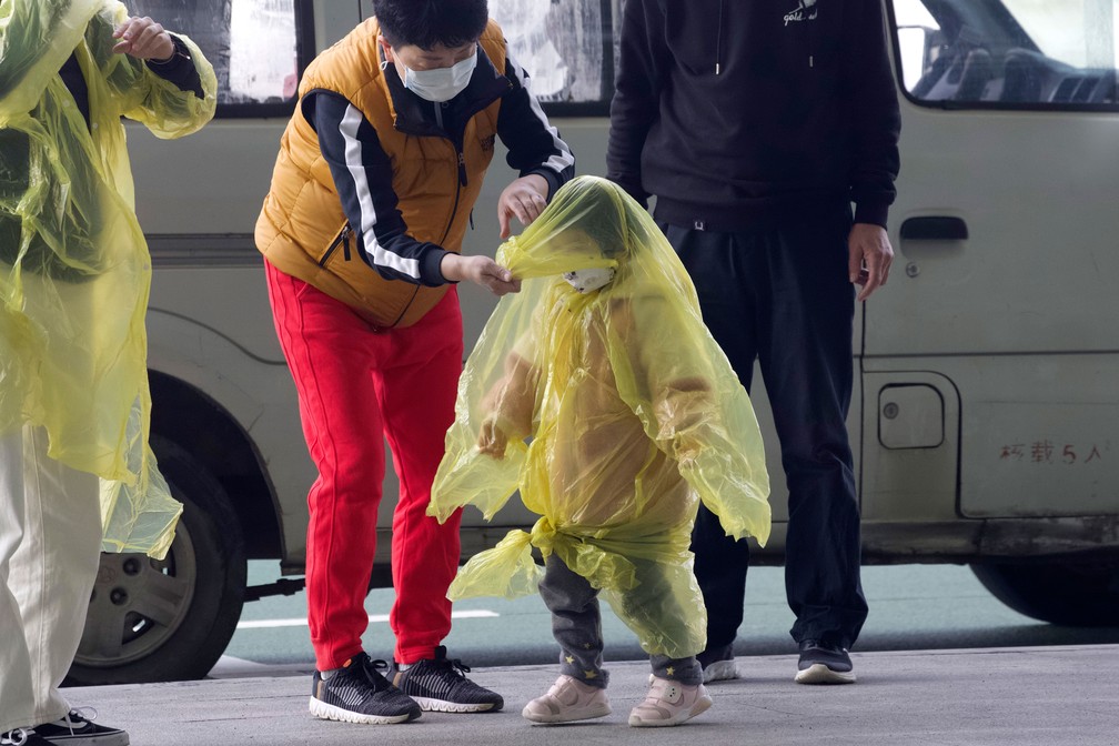 Mulher com máscara improvisa cobertura para proteger crianças de contaminação pelo novo coronavírus em aeroporto de Wuhan, na China, nesta quarta-feira (8) — Foto: Han Han Guan/AP 