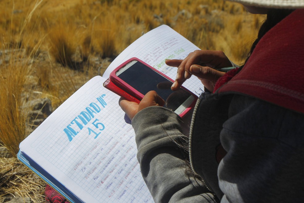 24 de julho de 2020 - estudante faz notas no caderno enquanto acessa as aulas remotas pelo celular, no Peru. País estima que 300 mil alunos possam abandonar a escola ou desistir dos estudos por causa da pandemia — Foto: Carlos Mamani / AFP