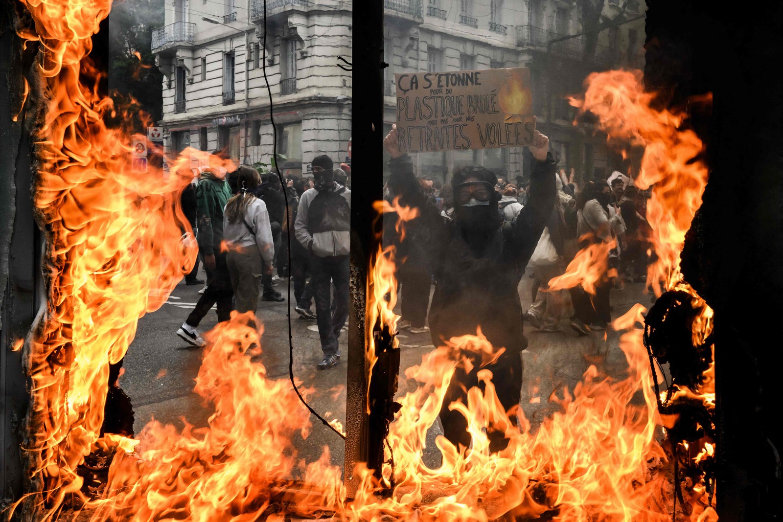 Manifestante é visto através de uma vitrine em chamas durante ato marcado por confrontos em Lyon — Foto: JEFF PACHOUD / AFP