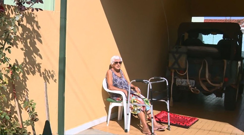 Dona Rosalina, de Indaiatuba, toma sol em frente ao carro que tenta transferir para o nome da bisneta — Foto: Vanderlei Duarte/EPTV