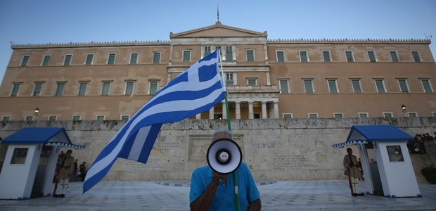 Homem carrega bandeira da Grécia e usa megafone para criticar o governo diante do Parlamento grego em Atenas, antes da assinatura de novas medidas de austeridade para permanecer na zona do euro (Foto: Christopher Furlong/Getty Images)