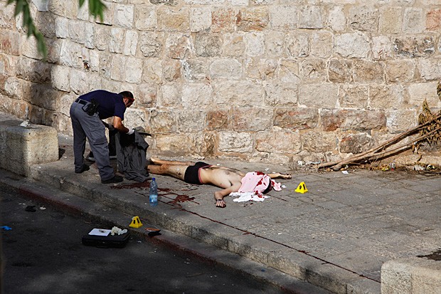 Policial recolhe pertences de agressor morto a tiros no Portão dos Leões, em Jerusalém (Foto: Mahmoud Illean/AP)