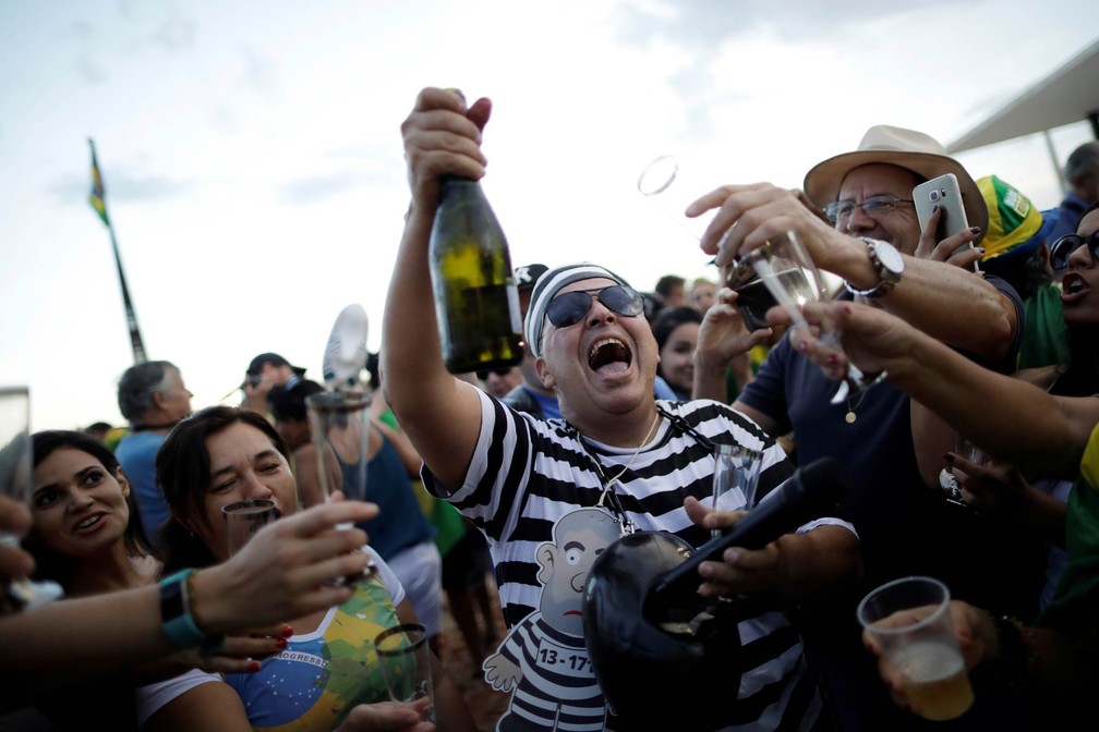 Manifestantes contrários a Lula, um deles fantasiado de presidiário, tomam champanhe comemorando a condenação do ex-presidente na Praça dos Três Poderes, em Brasília (Foto: Ueslei Marcelino/Reuters)