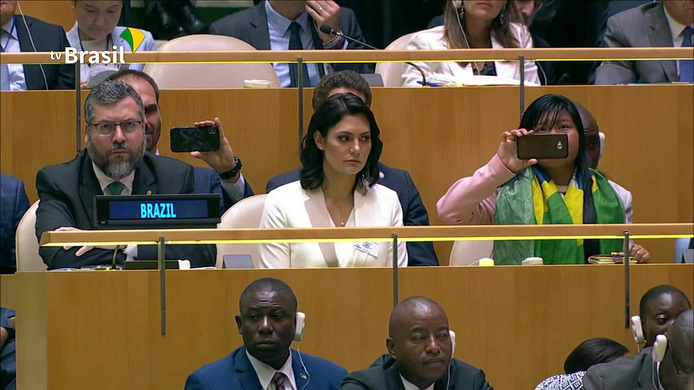 O chanceler Ernesto Araújo acompanha o discurso do presidente ao lado da primeira-dama, Michelle Bolsonaro, e da mulher indígena Ysani Kalapalo. — Foto: Reprodução