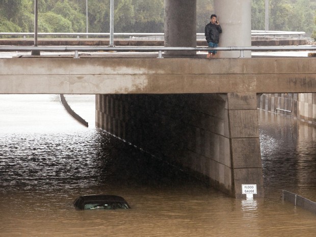 Motorista do Uber fala ao celular perto de seu carro inundado por enchente em Houston, Texas, neste domingo (25) (Foto: Reuters/Daniel Kramer)