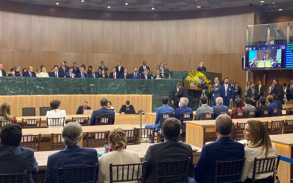 Na mesa, o vice-governador Daniel Vilela e deputados estaduais de Goiás; no telão à direita, o governador Ronaldo Caiado posicionado para posse, em Goiásnado — Foto: Vitor Santana/g1 