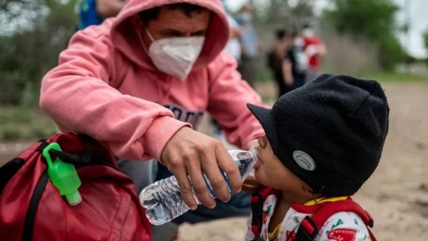 Um imigrante dá água à sua filha perto da fronteira EUA-México em Del Rio, Texas. Foto tirada em 16 de maio de 2021 (Foto: SERGIO FLORES/AFP VIA GETTY IMAGES via BBC)