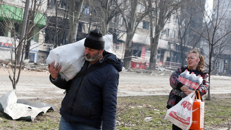 Moradores locais carregam alimentos enquanto passam por um prédio de apartamentos danificado em Mariupol, Ucrânia (Foto: REUTERS/Alexander Ermochenko)