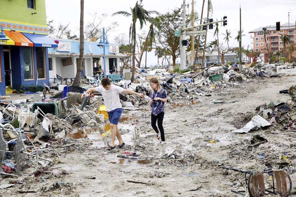 Jovens atravessam área destruída pela passagem do furacão Ian na praia de Fort Myers, na Flórida — Foto: Douglas R. Clifford/Tampa Bay Times via AP