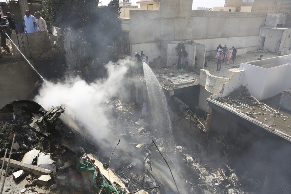 Bombeiros tentam controlar fogo causado pela queda de um avião comercial na área residencial de Karachi, no Paquistão — Foto: Fareed Khan/AP
