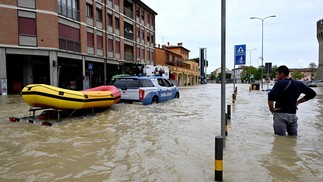 Homem observa carro da polícia que transporta um bote em uma rua inundada na cidade de Lugo — Foto: Andreas SOLARO / AFP