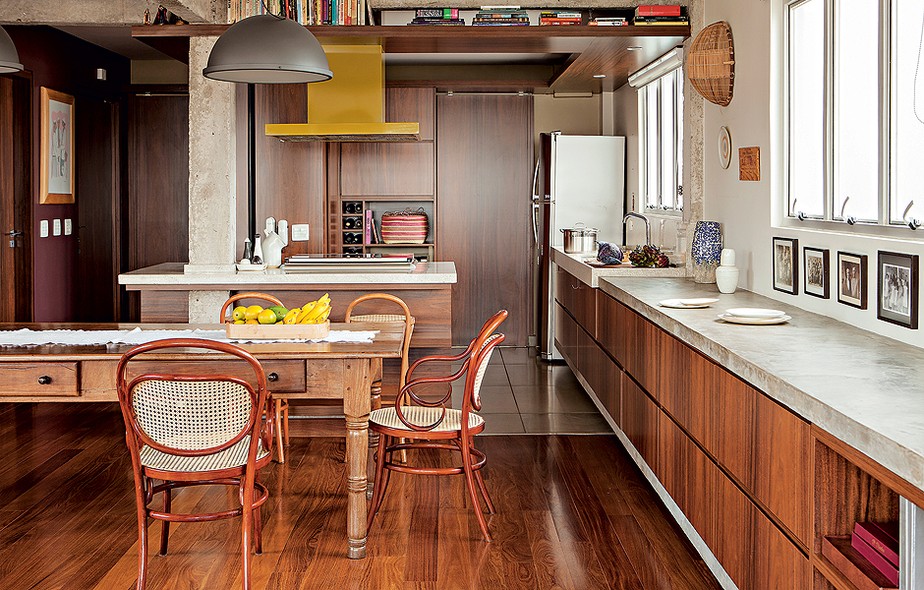 O projeto do arquiteto Gustavo Calazans tem cozinha escancarada, sem nenhum divisória com o resto da casa. A mesa de jantar é de madeira escura, semelhante aos móveis embutidos