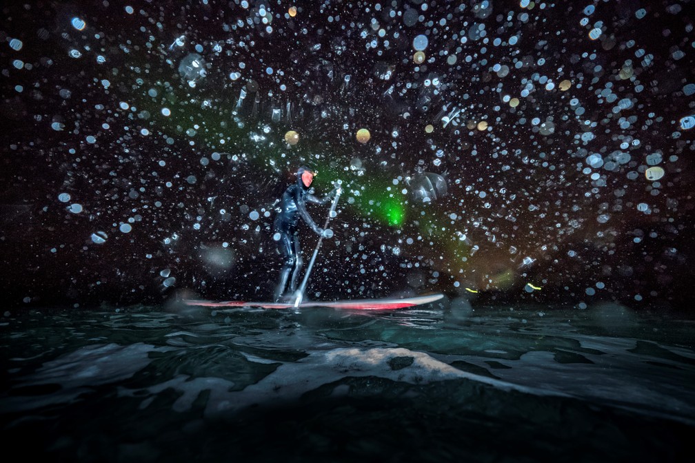 Tem gente que prefere surfar à noite para observar as luzes da aurora boreal (Foto: Olivier Morin/AFP)