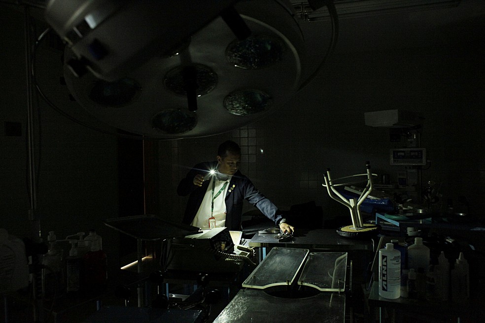 Enfermeiro usa luz de telefone celular ao manusear material em hospital em Rubio, na Venezuela (Foto: Carlos Eduardo Ramirez/Reuters)
