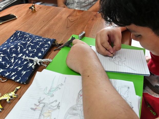 See Toh Sheng Jie desenha dinossauros em sua casa em Cingapura, na sexta (5), ao lado de algumas bolsas ilustradas por ele e iguais à usada por Lee Hsien Loong, mulher do primeiro-ministro (Foto: Roslan Rahman/AFP) See Toh Sheng Jie desenha dinossauros em sua casa em Cingapura, na sexta (5), ao lado de algumas bolsas ilustradas por ele e iguais à usada por Lee Hsien Loong, mulher do primeiro-ministro (Foto: Roslan Rahman/AFP)