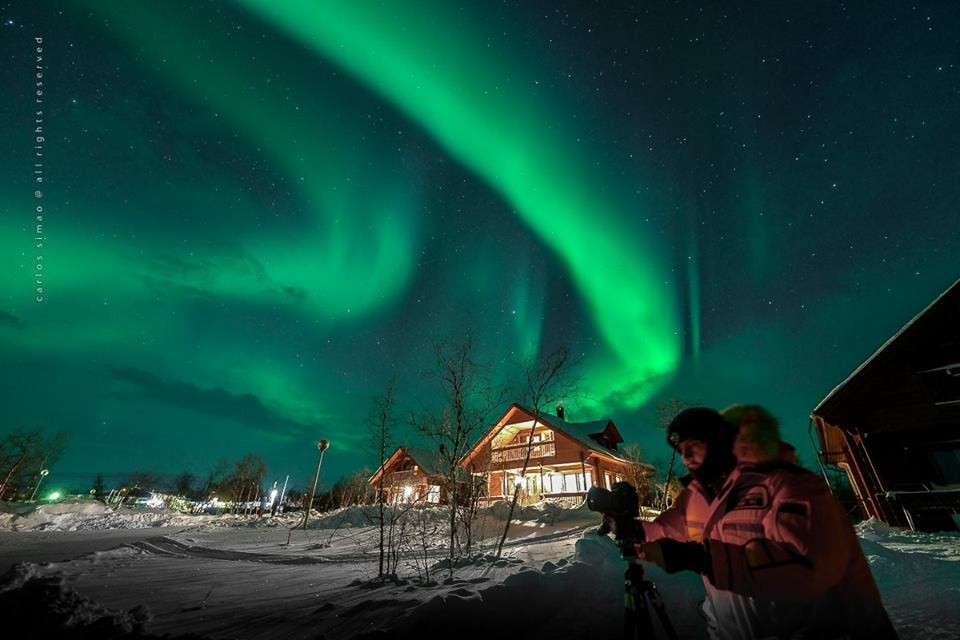 Marco prepara uma foto em meio à aurora em frente a um chalé no Ártico (Foto: Divulgação)