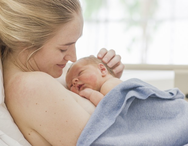 Mãe sorrindo com recém nascido no colo (Foto: Getty Images)