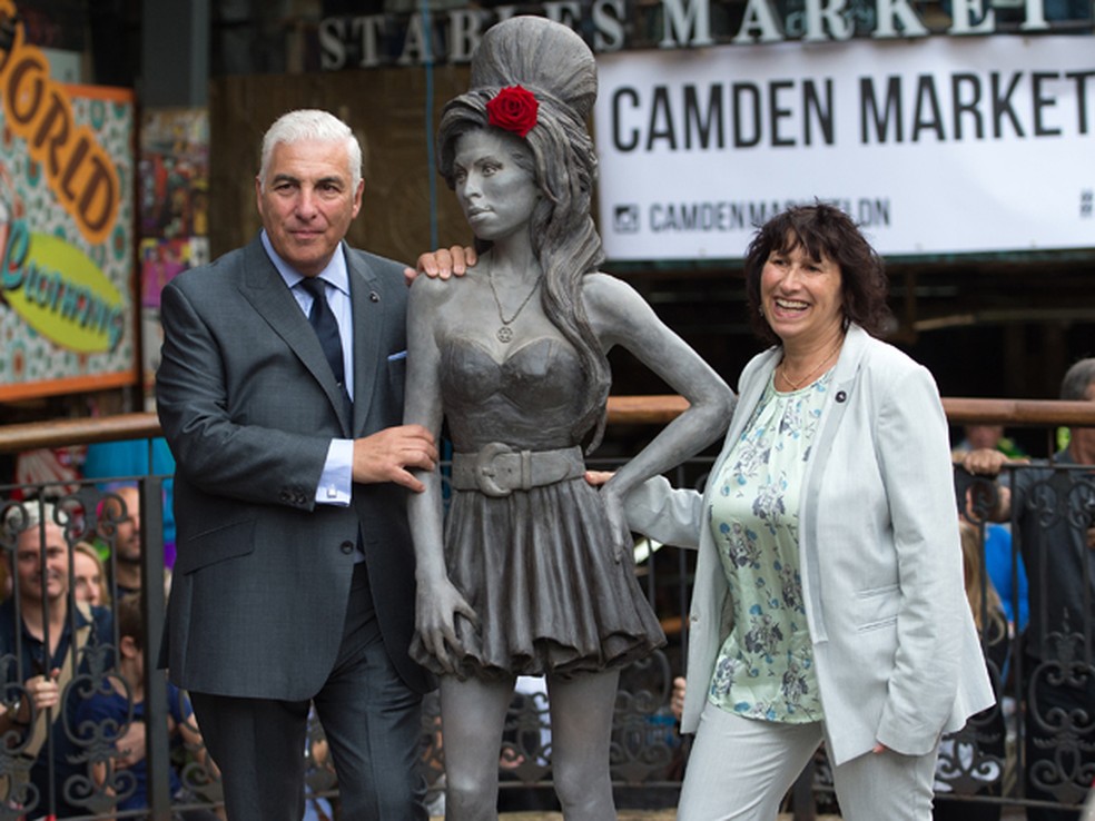 Os pais de Amy Winehouse, Mitch e Janis, posam ao lado de estátua em homenagem à cantora, que foi inaugurada neste domingo (14) no Camden's Stables Market, bairro de Londres — Foto: AP Photo/Tim Ireland