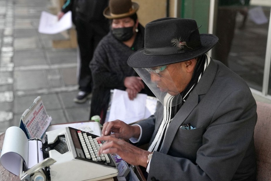 O datilógrafo Rogelio Condori digita em uma máquina de escrever ao lado de uma indígena aimara na rua em La Paz