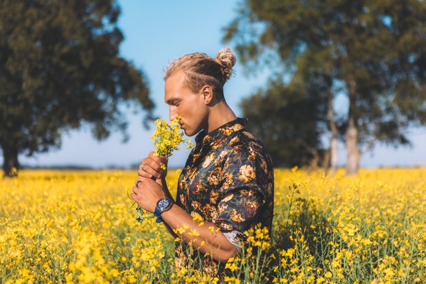 Curly blond guy is standing at the field and sniffs a flowers. Romantic, summer time. (Foto: Getty Images)