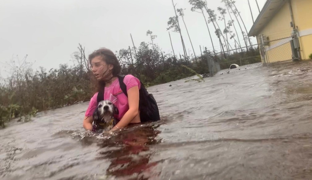 Julia Aylen atravessa as ruas alagadas carregando seu cachorro de estimação enquanto é resgatada de sua casa inundada durante passagem do furacão Dorian, em Freeport, nas Bahamas — Foto: Tim Aylen/AP