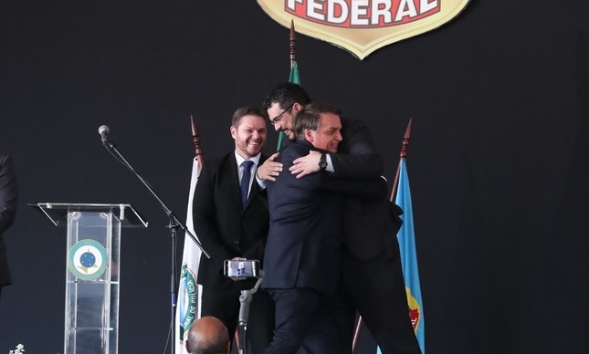 O papiloscopista João Paulo Dondelli abraça Bolsonaro ao lado do agente Danilo Campetti, todos sem máscara, durante solenidade da PF em outubro de 2020