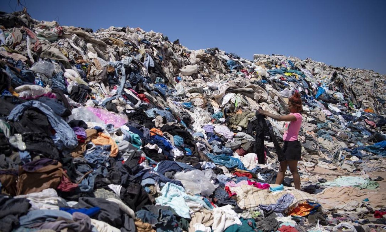 Mulher procura por roupas que lhe sirvam em meio a toneladas descartadas no deserto do Atacama  — Foto: MARTIN BERNETTI / AFP