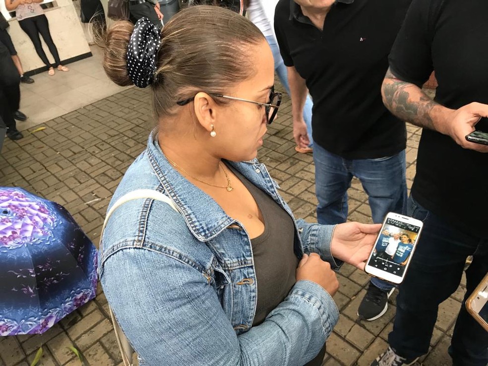 Valdênia Evangelista, na porta do Hospital, mostra a foto do sobrinho morto após ser espancado por colega — Foto: Pedro Angelo/G1