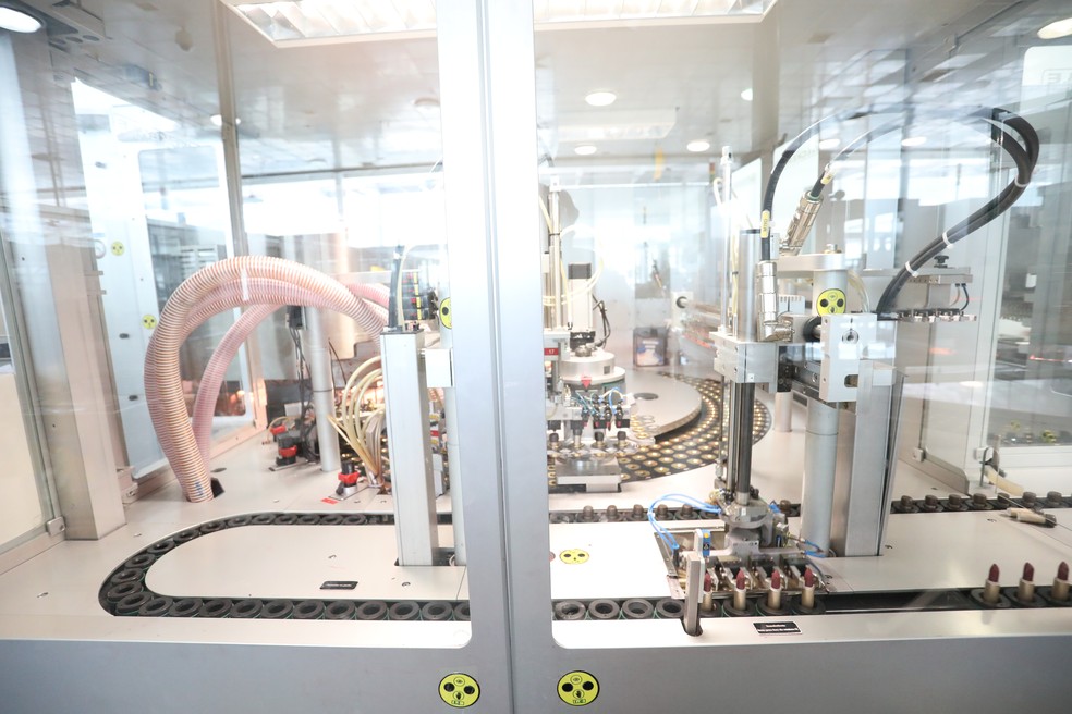 O batom líquido despejado nos moldes é resfriado em segundos. A máquina os encaixa nas bases de plástico e, em seguida, os batons seguem na esteira em posição vertical (Foto: Celso Tavares/G1)