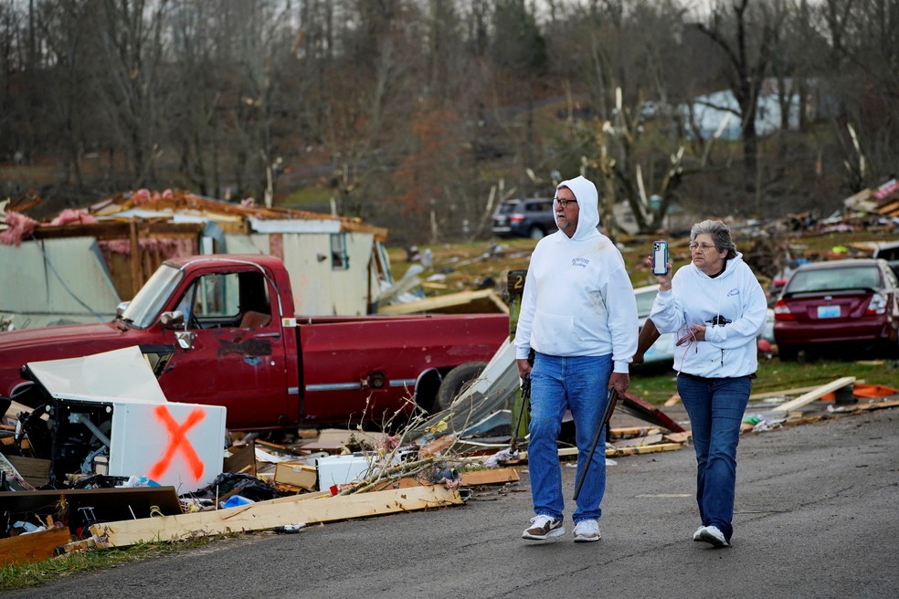 Bill Mosley caminha com sua esposa Bonnie carregando duas de suas armas, os únicos itens que ele conseguiu recuperar depois que sua casa foi destruída pela passagem de um tornado em Kentucky, nos EUA — Foto: Cheney Orr/Reuters