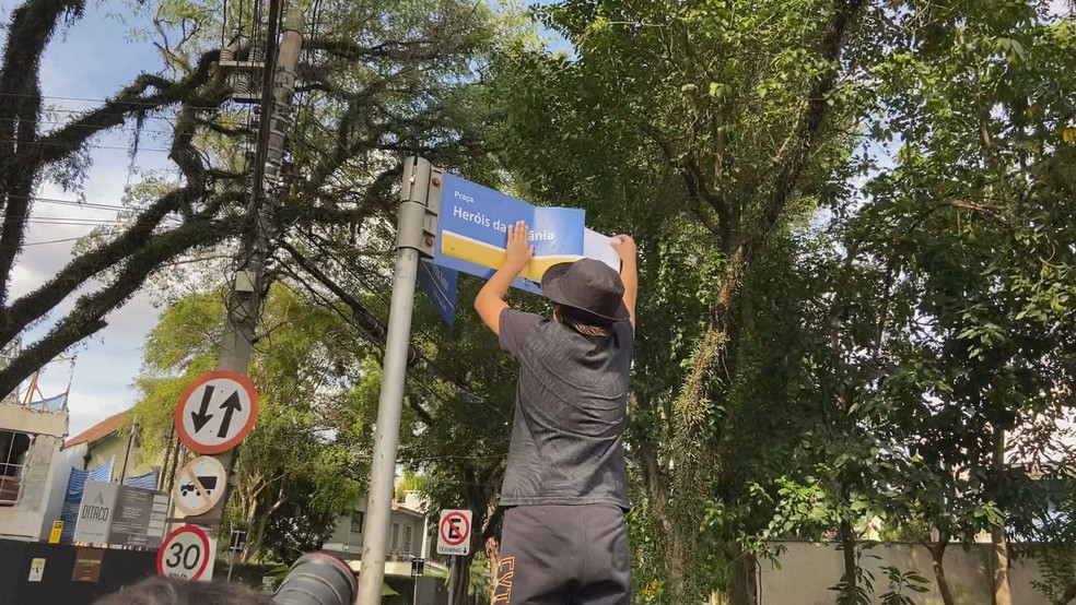 Manifestante cola adesivo: 'Heróis da Ucrânia' sobre placa da Rua Rússia — Foto: Reprodução/TV