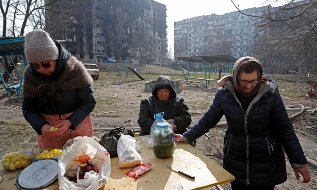 Ucranianos fazem refeição em frente a prédios bombardeados em Mariupol