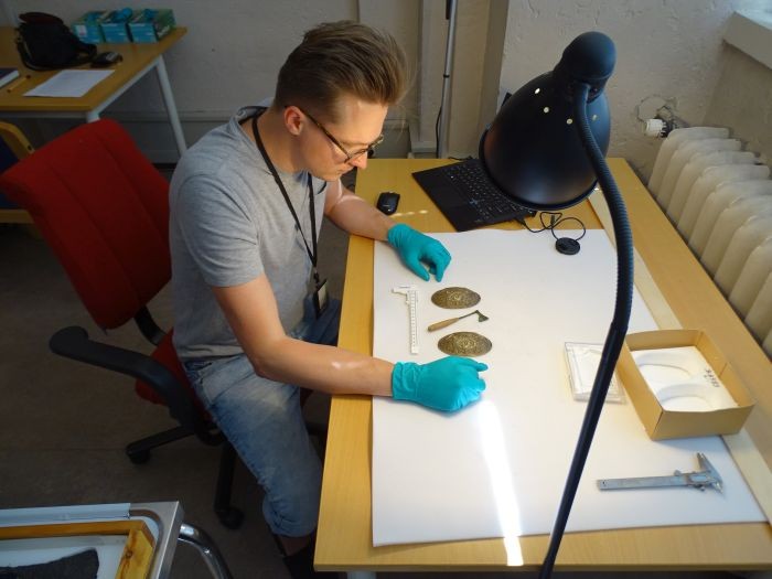 Leszek Gardeła analisa machado em miniatura e jóia encontrada em uma tumba na Noruega  (Foto: Poland's Ministry of Science and Higher Education)