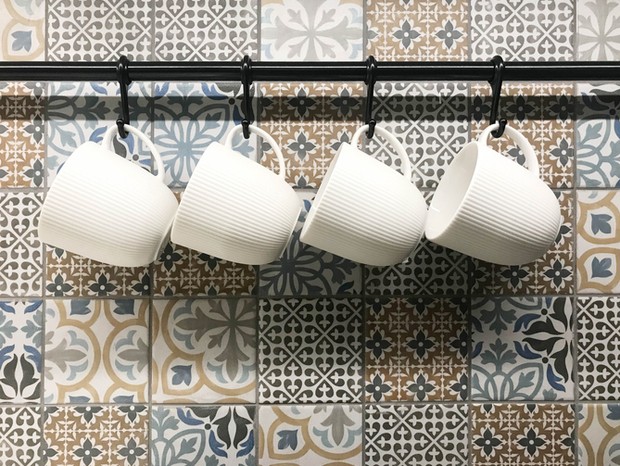 White ceramic cups hanging on hook in front of art pattern tile wall, in coffee shop or kitchenware store (Foto: Getty Images/iStockphoto)