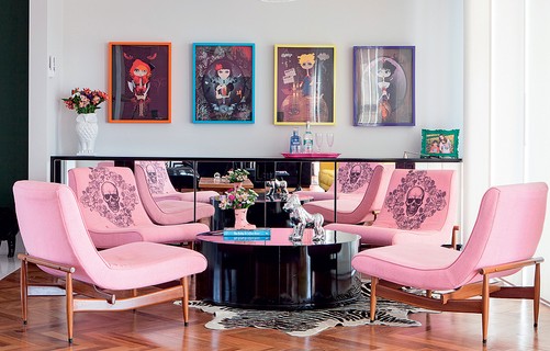 No espaço onde ficaria a mesa de jantar, a arquiteta Andrea Murao criou um lounge com mesa de centro baixa e aparador espelhado. A modernidade ficou por conta das cores usadas, como o rosa das cadeiras, os quadros e as caveiras