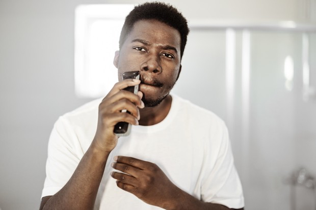 Portrait of young african american man shaving with trimmer (Foto: Getty Images)