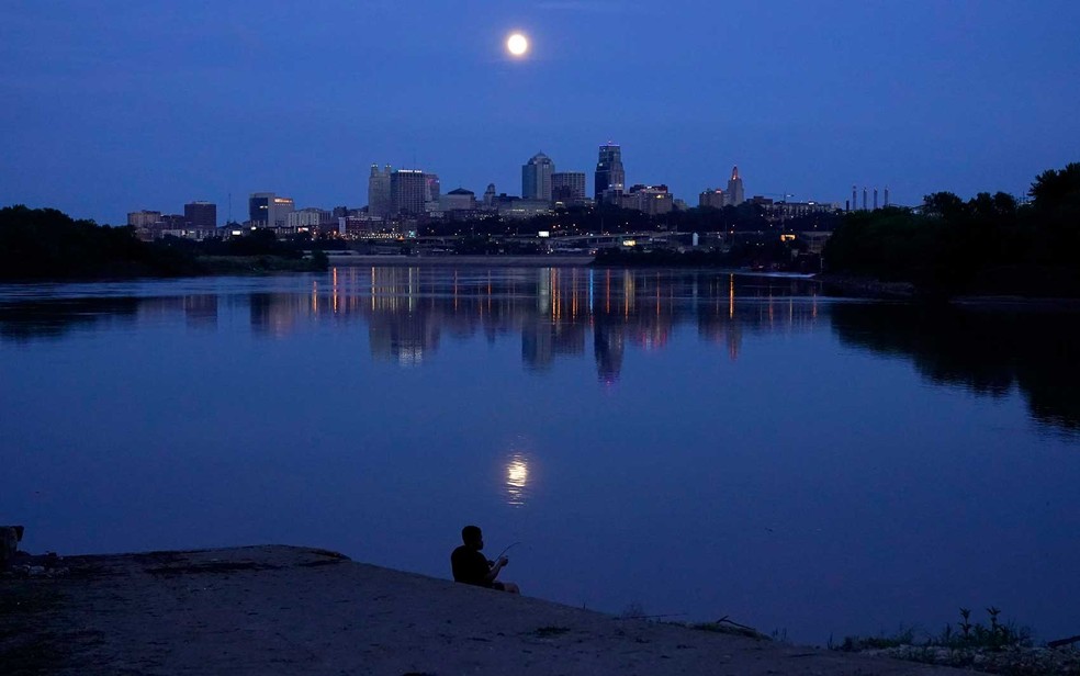 Homem pesca no rio Missouri enquanto a lua quase cheia sobe al�m do horizonte em Kansas City, Missouri � Foto: Charlie Riedel / AP Photo
