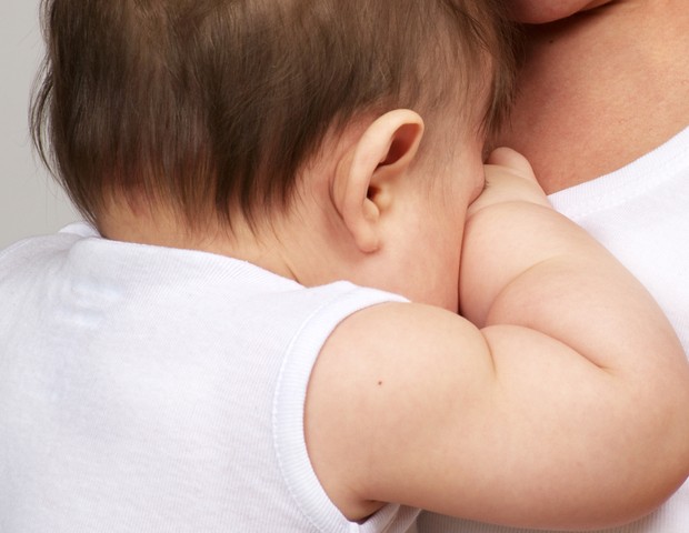 Bebê com cólica no colo da mãe (Foto: Shutterstock)