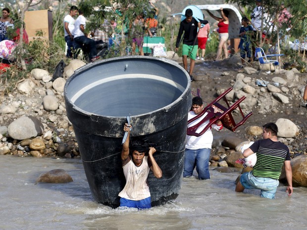 Colombianos carregam seus pertences ao cruzar a fronteira do rio San Antonio del Tachira, na Venezuela, até Villa del Rosario, na Colômbia. Cerca de mil colombianos ilegais foram deportados durante uma operação na fronteira (Foto: Jose Miguel Gomez/Reuters)