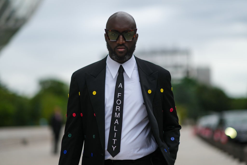 PARIS, FRANCE - JULY 05: Virgil Abloh wears a white shirt, a black tie with 'A Formality' slogan, a black blazer jacket with multicolored buttons embroidered, black flared suit pants, a gold watch, butterfly sunglasses, outside Louis Vuitton Parfum hosts  (Foto: Getty Images)